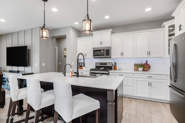 kitchen with white cabinetry, decorative light fixtures, a center island with sink, stainless steel appliances, and backsplash