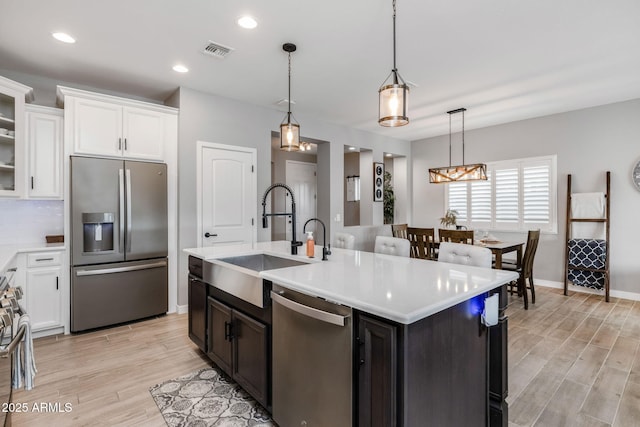 kitchen with sink, white cabinets, hanging light fixtures, stainless steel appliances, and a center island with sink