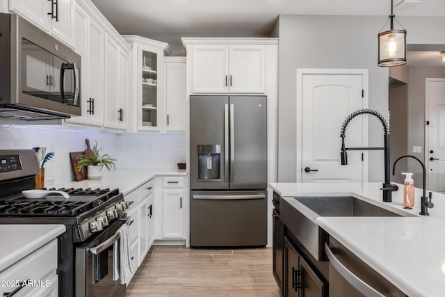 kitchen with sink, hanging light fixtures, appliances with stainless steel finishes, decorative backsplash, and white cabinets