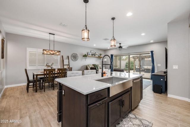 kitchen featuring dishwasher, sink, hanging light fixtures, light hardwood / wood-style floors, and a center island with sink