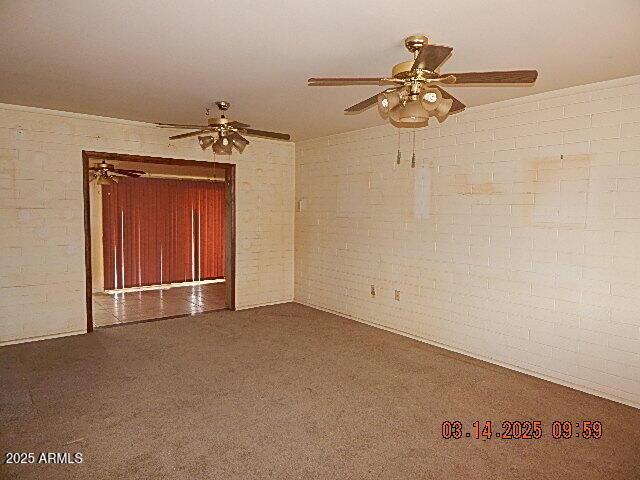 unfurnished room featuring carpet flooring, a ceiling fan, and brick wall