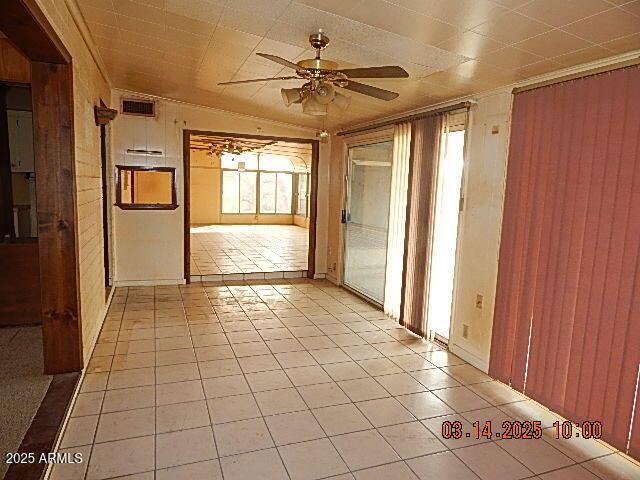 spare room featuring wooden walls, visible vents, ceiling fan, and light tile patterned floors