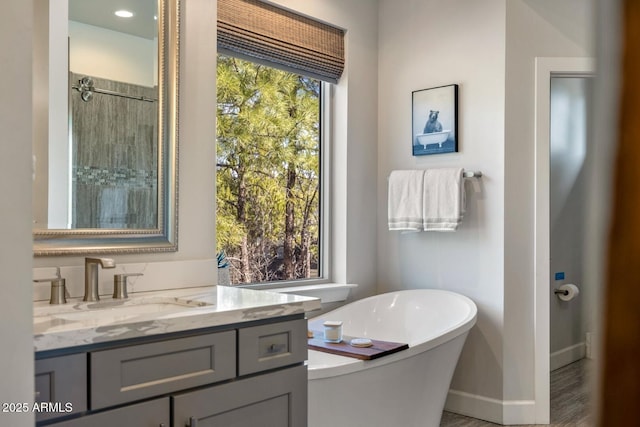 full bath featuring baseboards, a freestanding tub, tiled shower, and vanity