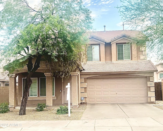 traditional home with concrete driveway, a tiled roof, an attached garage, fence, and stucco siding