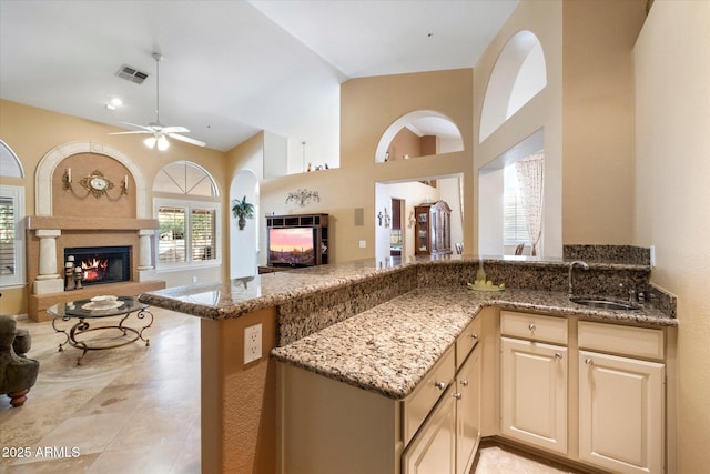 kitchen featuring high vaulted ceiling, stone countertops, kitchen peninsula, and sink