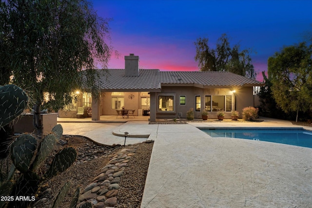 back house at dusk featuring a patio