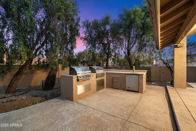 patio terrace at dusk featuring area for grilling and exterior kitchen