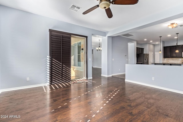 unfurnished living room featuring ceiling fan with notable chandelier and dark wood-type flooring