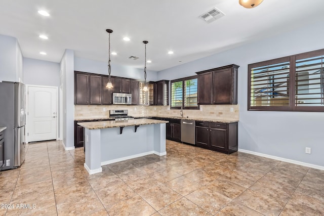 kitchen with light stone countertops, dark brown cabinets, stainless steel appliances, pendant lighting, and a center island