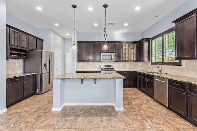 kitchen with tasteful backsplash, decorative light fixtures, dark brown cabinets, a kitchen island, and appliances with stainless steel finishes