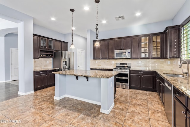 kitchen with light stone countertops, sink, pendant lighting, a kitchen island, and appliances with stainless steel finishes