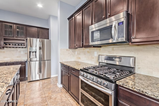 kitchen featuring decorative backsplash, light stone countertops, dark brown cabinets, and stainless steel appliances