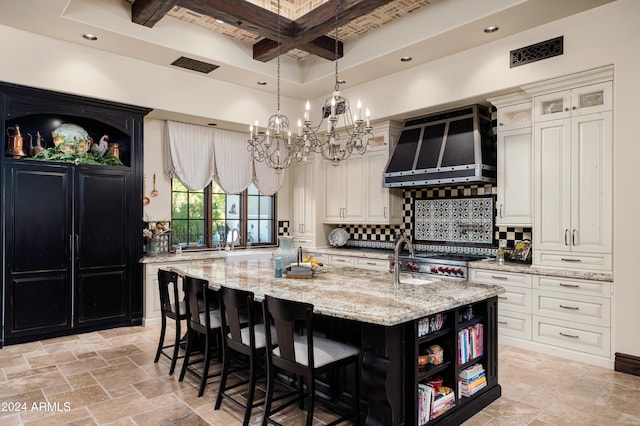 kitchen with a kitchen island with sink, wall chimney exhaust hood, light stone countertops, tasteful backsplash, and beam ceiling