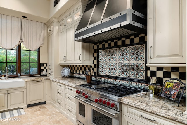 kitchen with range with two ovens, wall chimney range hood, light stone counters, and tasteful backsplash