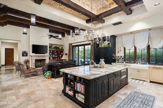 kitchen with beam ceiling, a center island with sink, light stone counters, and sink