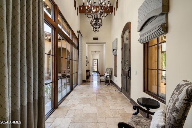 hall featuring a chandelier, a high ceiling, and a healthy amount of sunlight