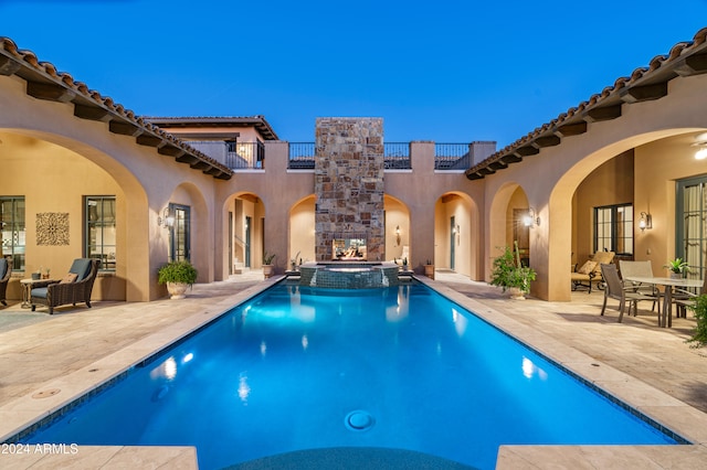 pool at dusk with an in ground hot tub and a patio area