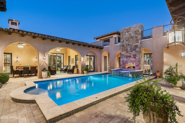 pool at dusk with an outdoor living space with a fireplace, a patio area, and an in ground hot tub