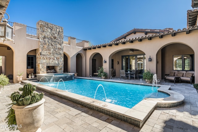 view of swimming pool featuring pool water feature, ceiling fan, an outdoor stone fireplace, an in ground hot tub, and a patio