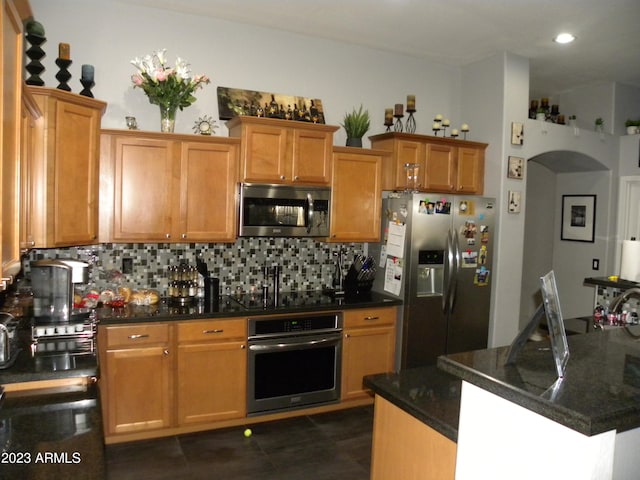 kitchen with dark tile flooring, tasteful backsplash, stainless steel appliances, a kitchen island, and dark stone counters