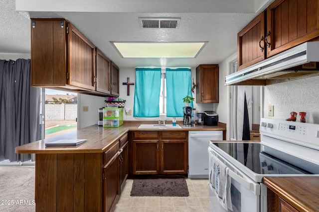 kitchen with a textured ceiling, under cabinet range hood, white appliances, a sink, and visible vents