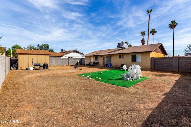 back of house with central air condition unit, a storage shed, a fenced backyard, and an outbuilding