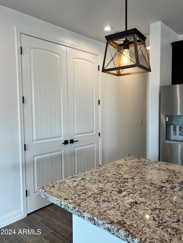 kitchen with stainless steel fridge with ice dispenser, dark wood-type flooring, hanging light fixtures, and light stone counters