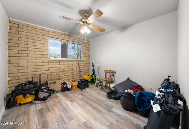 miscellaneous room featuring brick wall, light hardwood / wood-style floors, and ceiling fan