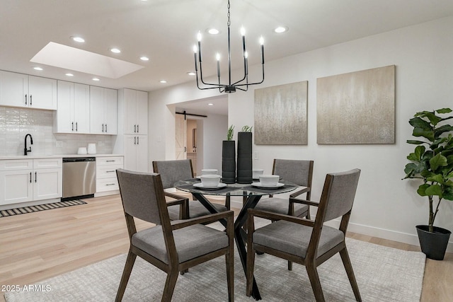 dining space with a barn door, a chandelier, sink, and light hardwood / wood-style floors