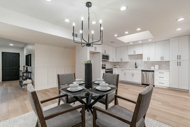 dining space with light hardwood / wood-style floors, an inviting chandelier, sink, and a skylight