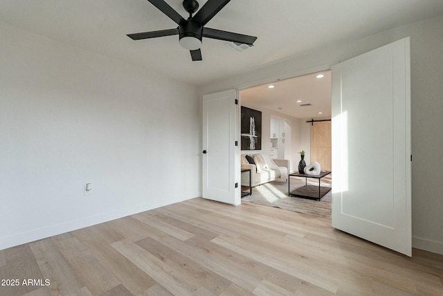 unfurnished room featuring ceiling fan, a barn door, and light wood-type flooring