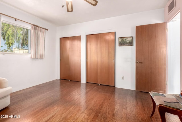 unfurnished bedroom featuring ceiling fan, multiple closets, wood finished floors, and visible vents