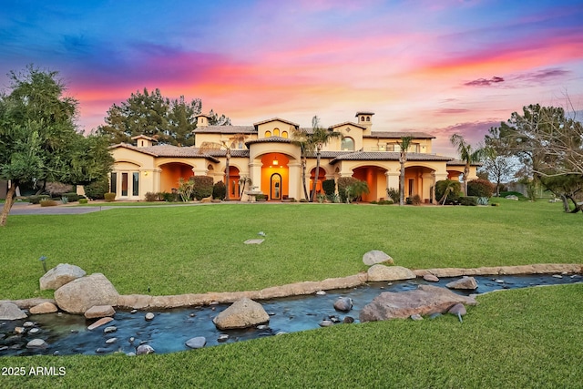 mediterranean / spanish house with stucco siding, a small pond, a tile roof, and a yard