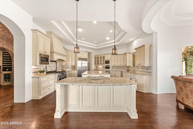 kitchen featuring cream cabinetry, a raised ceiling, custom exhaust hood, and built in appliances
