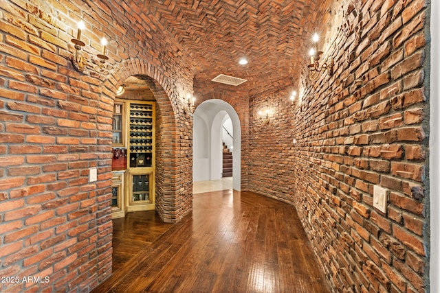 wine room with brick ceiling, arched walkways, brick wall, and hardwood / wood-style flooring