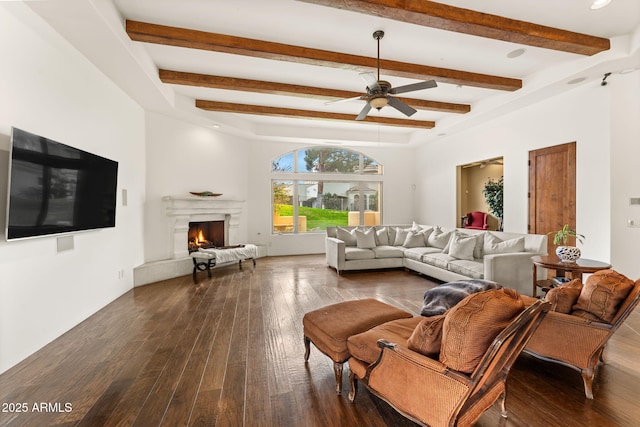 living area featuring a ceiling fan, a warm lit fireplace, wood-type flooring, and beam ceiling