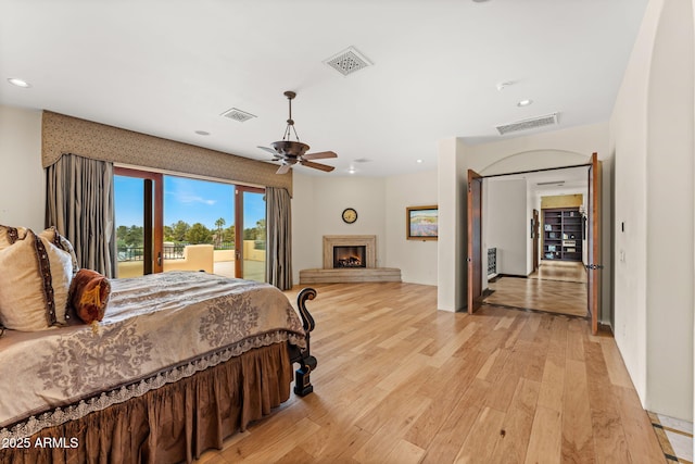 bedroom featuring a warm lit fireplace, light wood finished floors, visible vents, access to outside, and recessed lighting