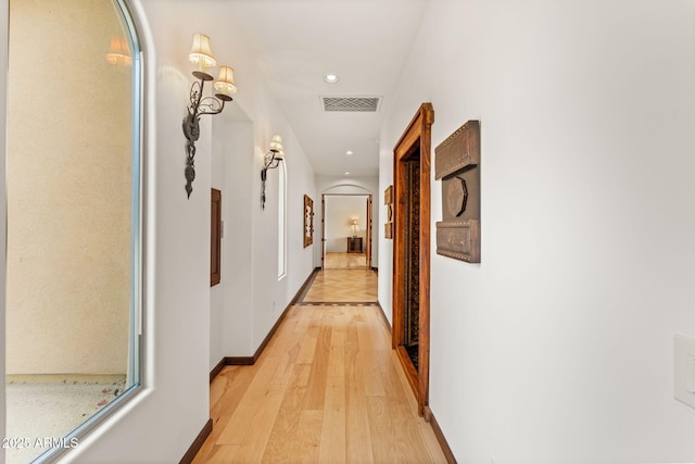 corridor featuring light wood finished floors, visible vents, arched walkways, baseboards, and recessed lighting