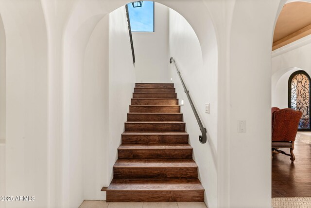 staircase featuring arched walkways and wood finished floors