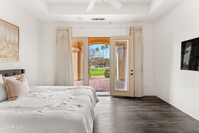 bedroom with access to outside, visible vents, a raised ceiling, and wood finished floors