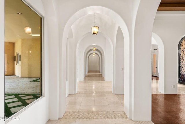 hallway featuring arched walkways and light tile patterned flooring