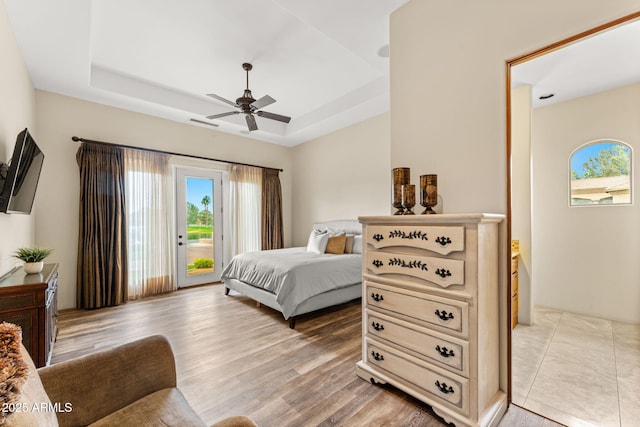 bedroom with light wood-type flooring, a tray ceiling, access to outside, and a ceiling fan