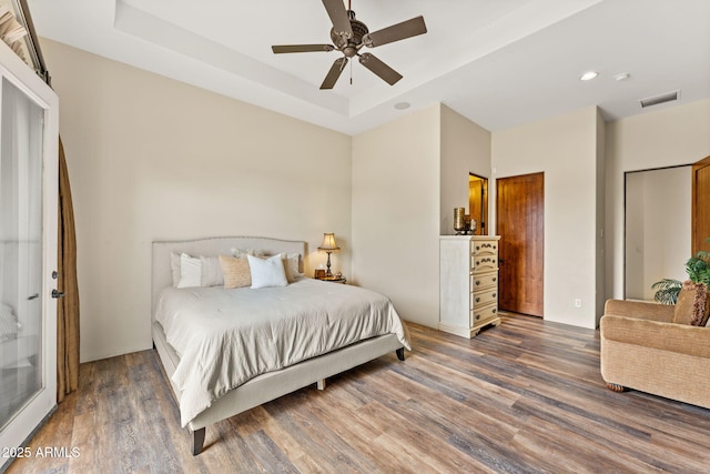 bedroom featuring a tray ceiling, visible vents, and wood finished floors