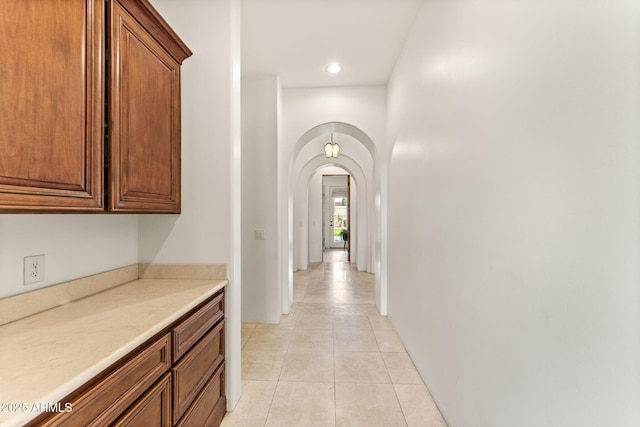 hallway with arched walkways, light tile patterned flooring, and recessed lighting