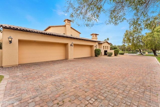 view of side of home with decorative driveway, an attached garage, and stucco siding