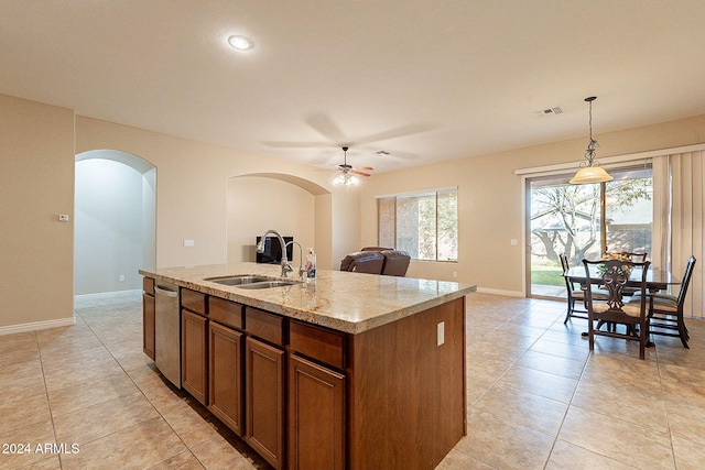 kitchen featuring light stone counters, ceiling fan, sink, pendant lighting, and an island with sink