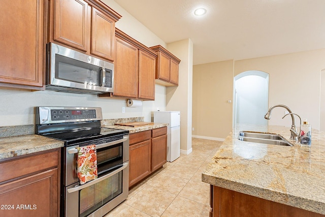 kitchen featuring appliances with stainless steel finishes, light tile patterned floors, light stone counters, and sink