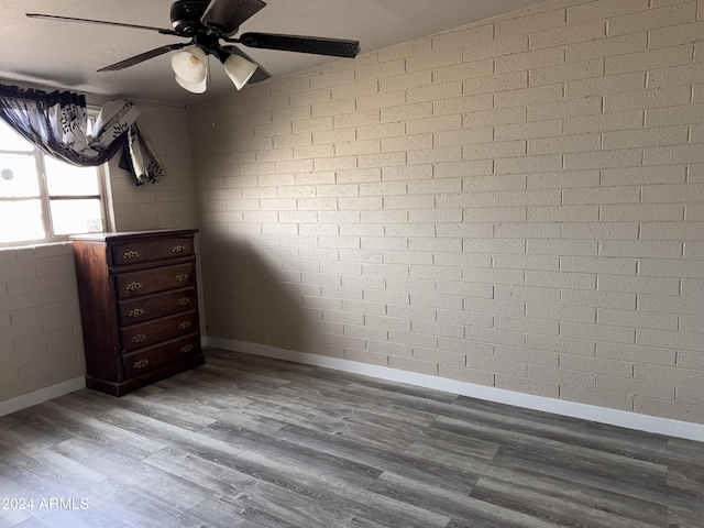 spare room with ceiling fan, brick wall, and wood-type flooring