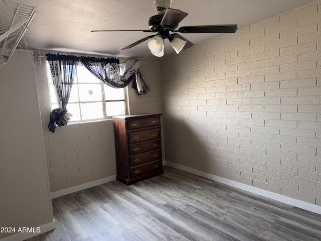 interior space with ceiling fan, hardwood / wood-style floors, brick wall, and a textured ceiling