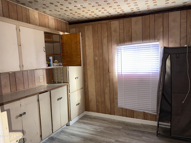 kitchen with white cabinetry, wooden walls, and light wood-type flooring